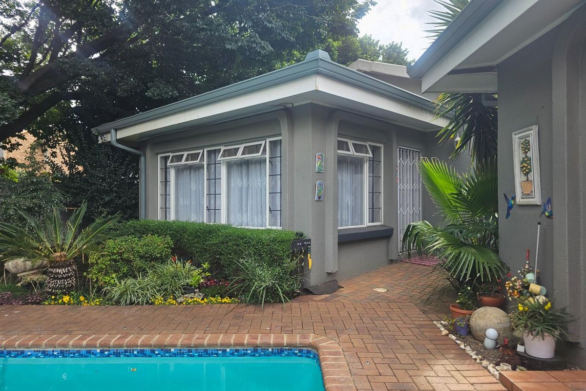A view of the rear exterior featuring a swimming pool, brick paved patio area, and a well-maintained garden surrounding the dwelling.