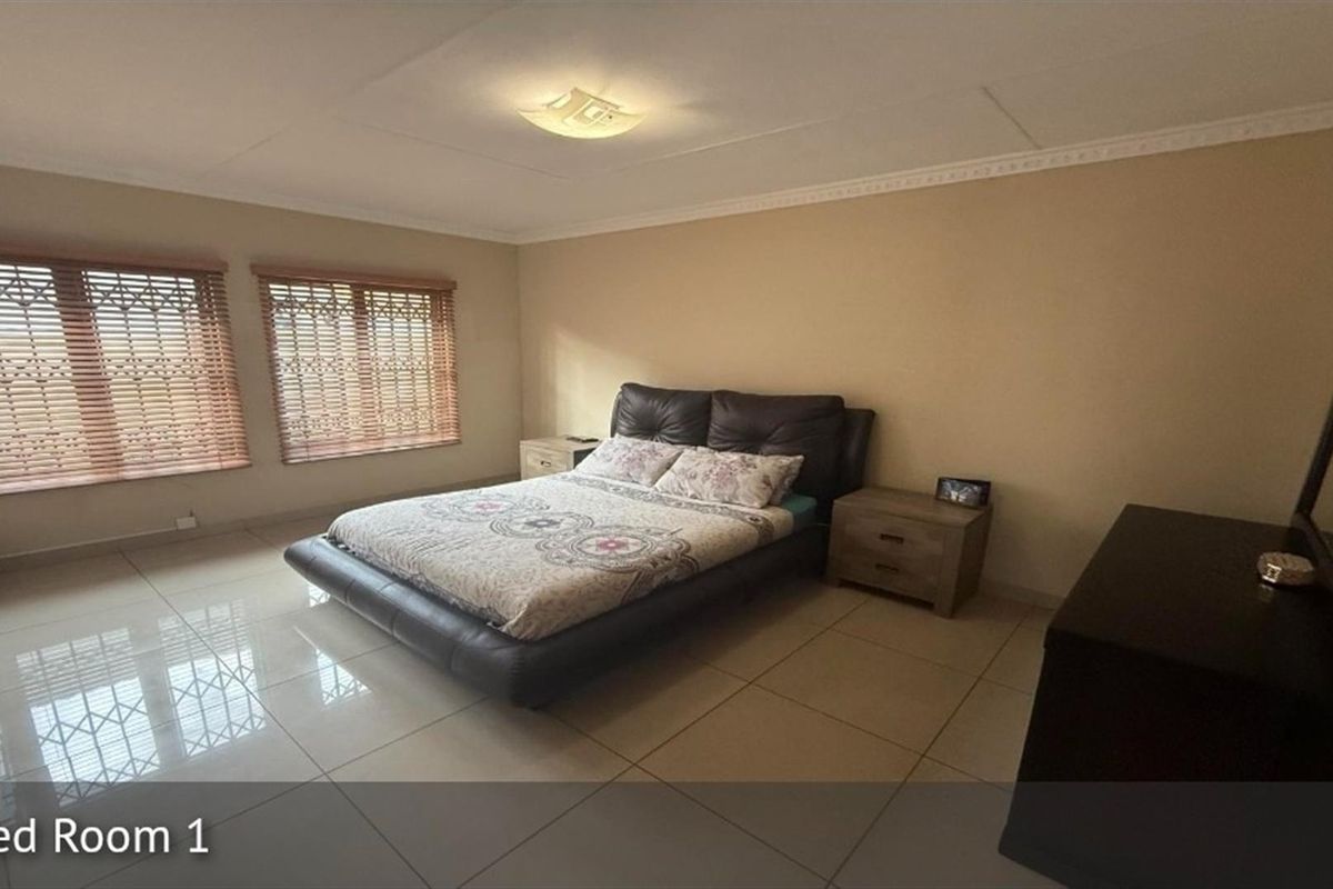Spacious bedroom featuring large format floor tiles, crown molding, and dual windows fitted with wooden blinds.