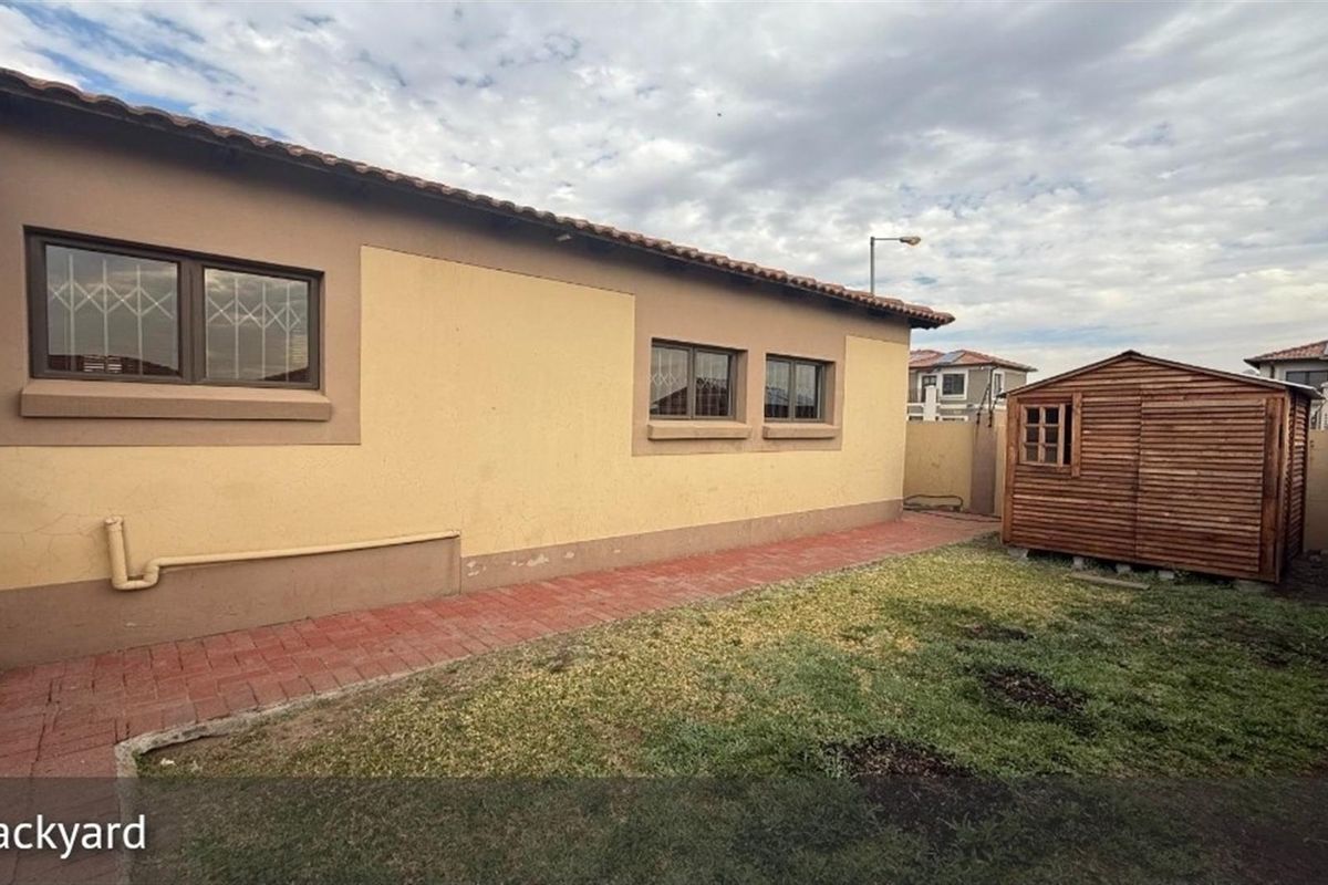 Rear exterior view of the property featuring a paved walkway, small lawn area, and a detached wooden storage shed.