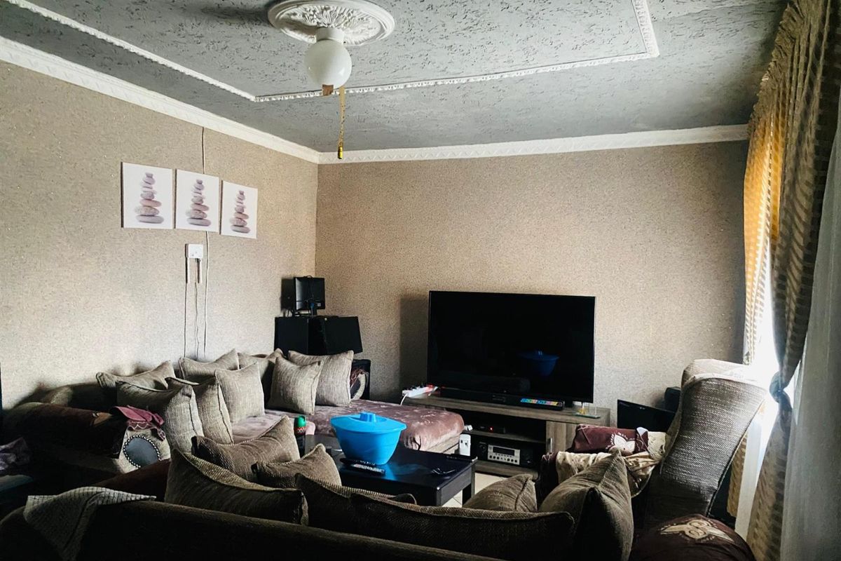 A living room featuring a textured ceiling with a decorative rose, neutral wall finishes, and large windows allowing natural light into the space.