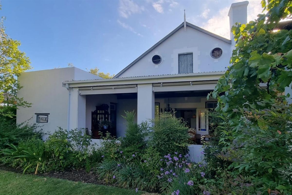 A view of the rear exterior of the house, featuring a covered patio area, landscaped garden, and traditional architectural details.
