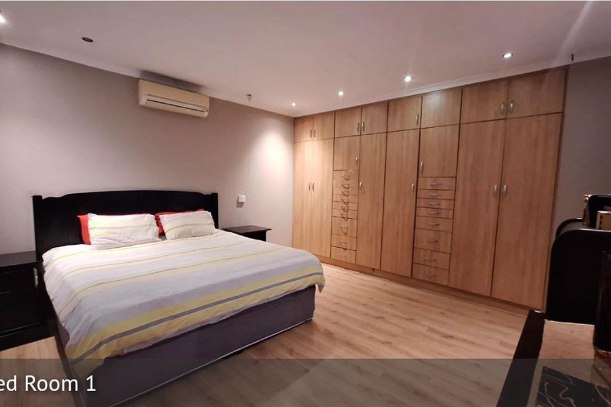 Spacious bedroom featuring light wood-look flooring, extensive built-in cabinetry, and a wall-mounted air conditioning unit.