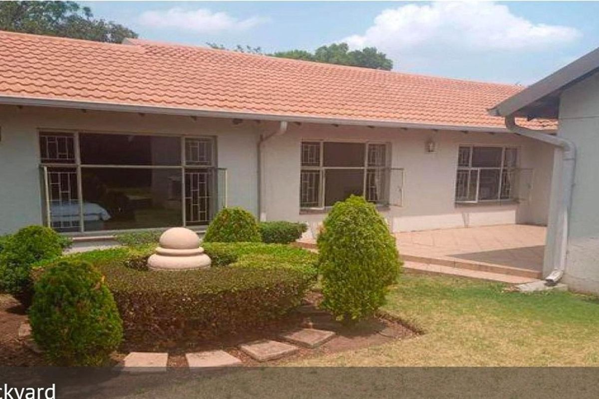 Rear view of the house featuring a tiled patio area, landscaped garden with a central feature, and large windows.