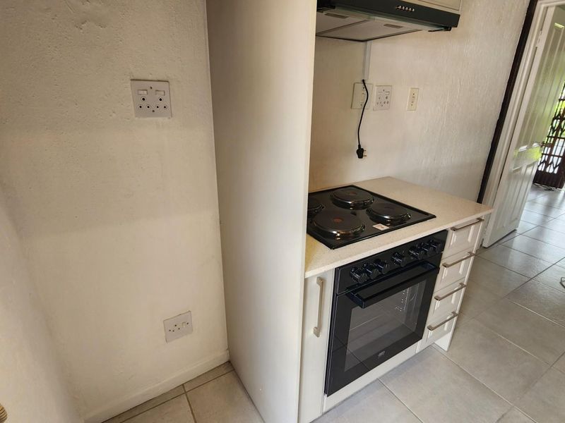 Compact kitchen area featuring built-in oven, electric hob, extractor fan, and tiled flooring, offering a functional space ready for modern updates.
