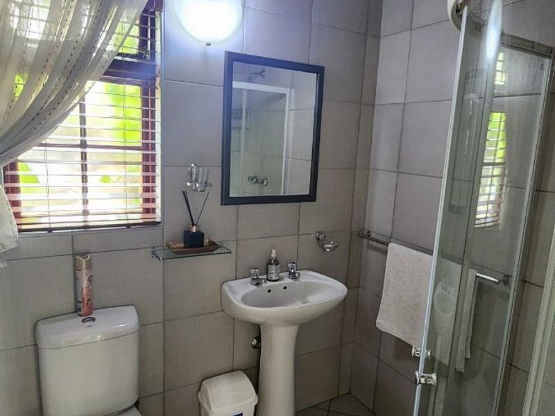 A functional bathroom featuring a pedestal basin, toilet, and glass shower enclosure, finished with tiled surfaces and a unique bamboo ceiling.
