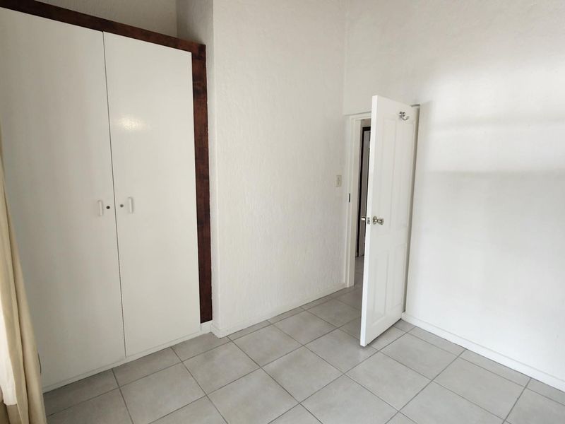 A clean, empty bedroom featuring neutral tiled flooring and a built-in wardrobe, offering a blank canvas for personalization.