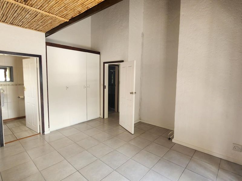 An empty bedroom featuring tiled flooring, built-in cupboards, and a unique exposed reed ceiling, with direct access to an adjoining bathroom.