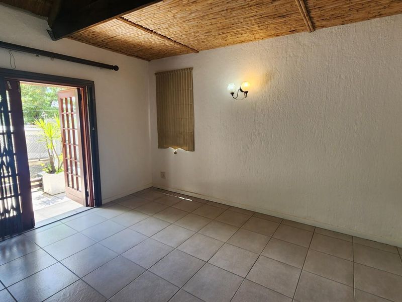 An empty living room featuring tiled flooring, a unique bamboo ceiling, and direct access to an outdoor area through a timber framed door.