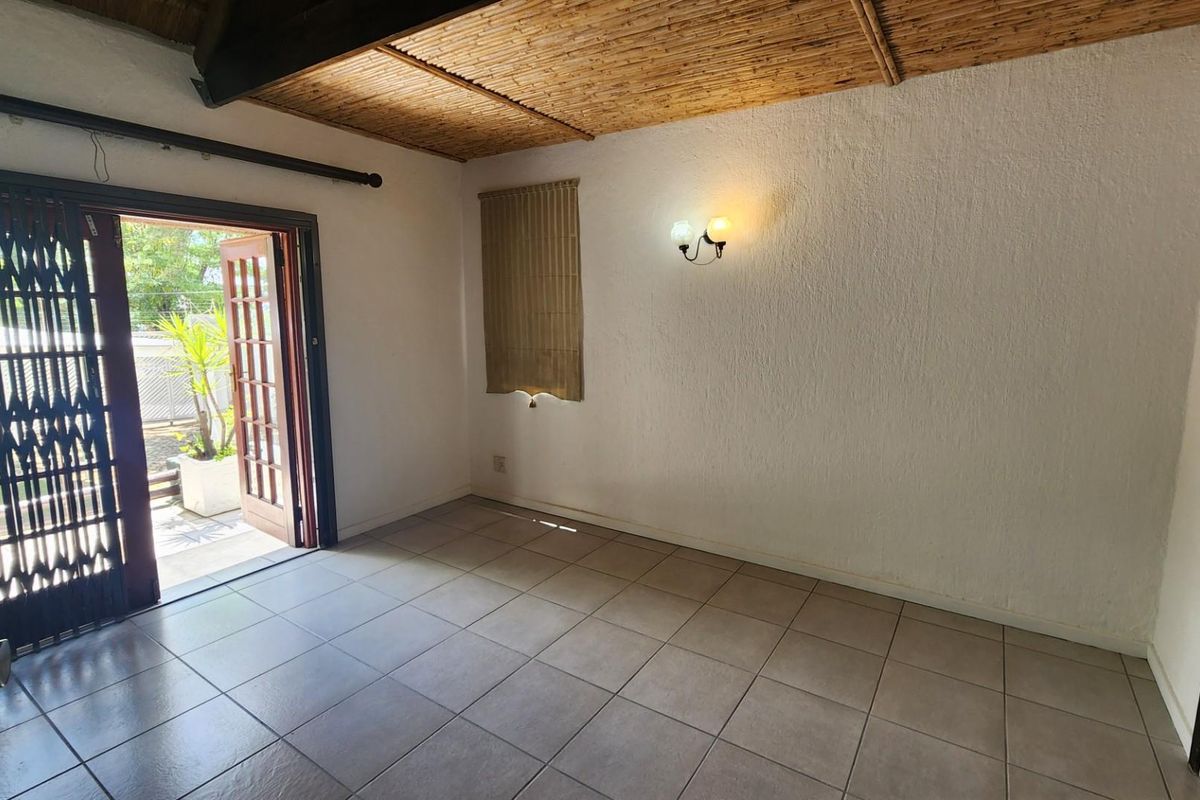 An empty living room featuring tiled flooring, a unique bamboo ceiling, and direct access to an outdoor area through a timber framed door.