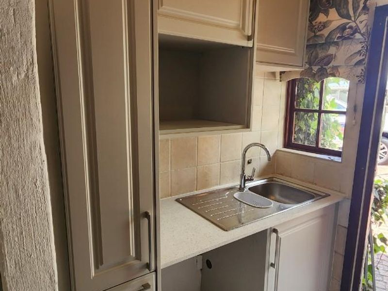 A compact scullery area featuring built-in cabinetry, a stainless steel sink, tiled splashback, and a distinctive timber ceiling.