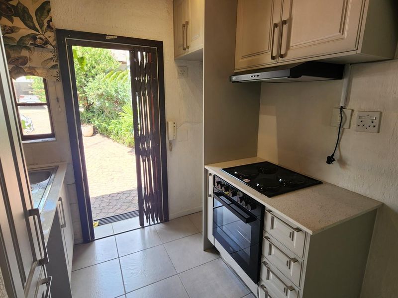 Compact kitchen featuring built-in cabinetry, electric hob, oven, extractor fan, and stone countertops, with direct access to an outdoor patio area.