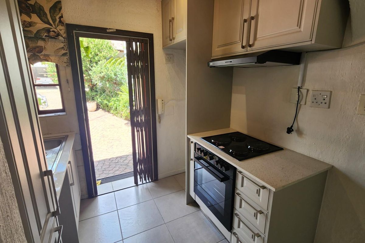 Compact kitchen featuring built-in cabinetry, electric hob, oven, extractor fan, and stone countertops, with direct access to an outdoor patio area.