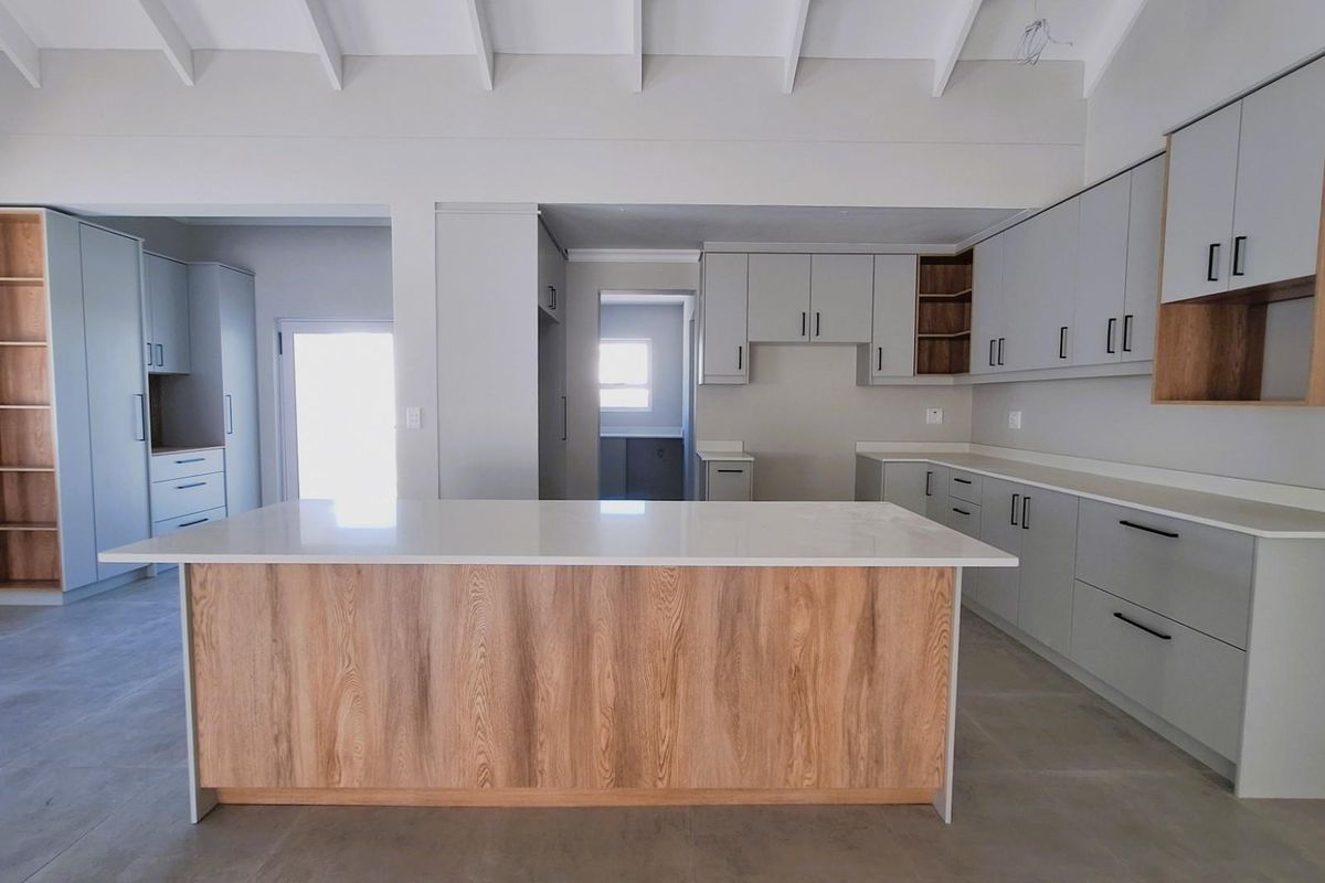 Modern open-plan kitchen featuring a central island, light grey cabinetry with wood-grain accents, stone countertops, and high vaulted ceilings.