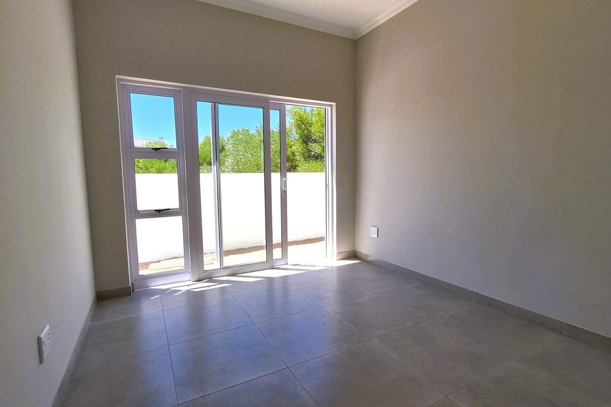 A bright, empty bedroom featuring neutral tiled flooring, clean walls, and large sliding glass doors providing direct access to the outdoor area.