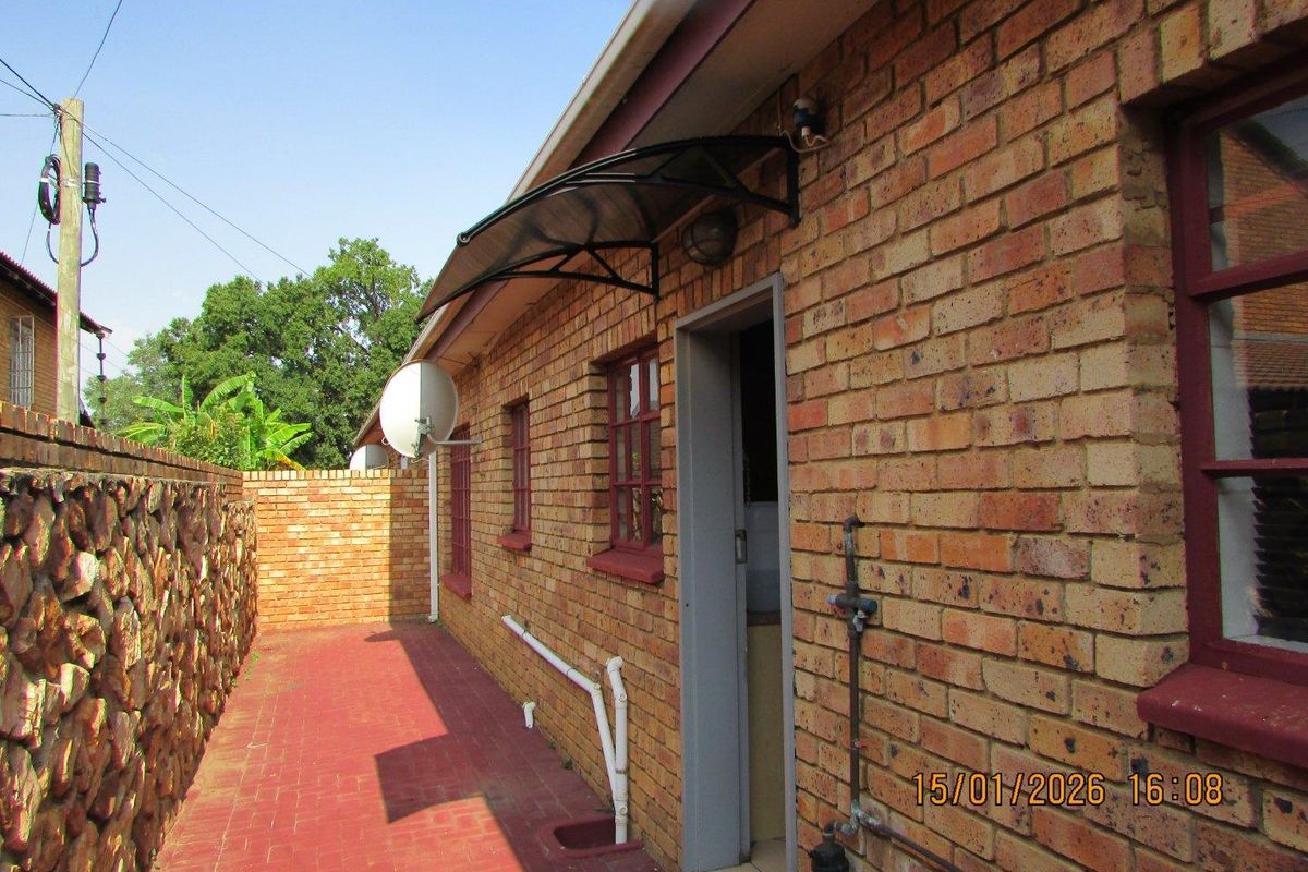 Side exterior view of the townhouse featuring face-brick walls, a paved walkway, and a protective awning over the entrance.
