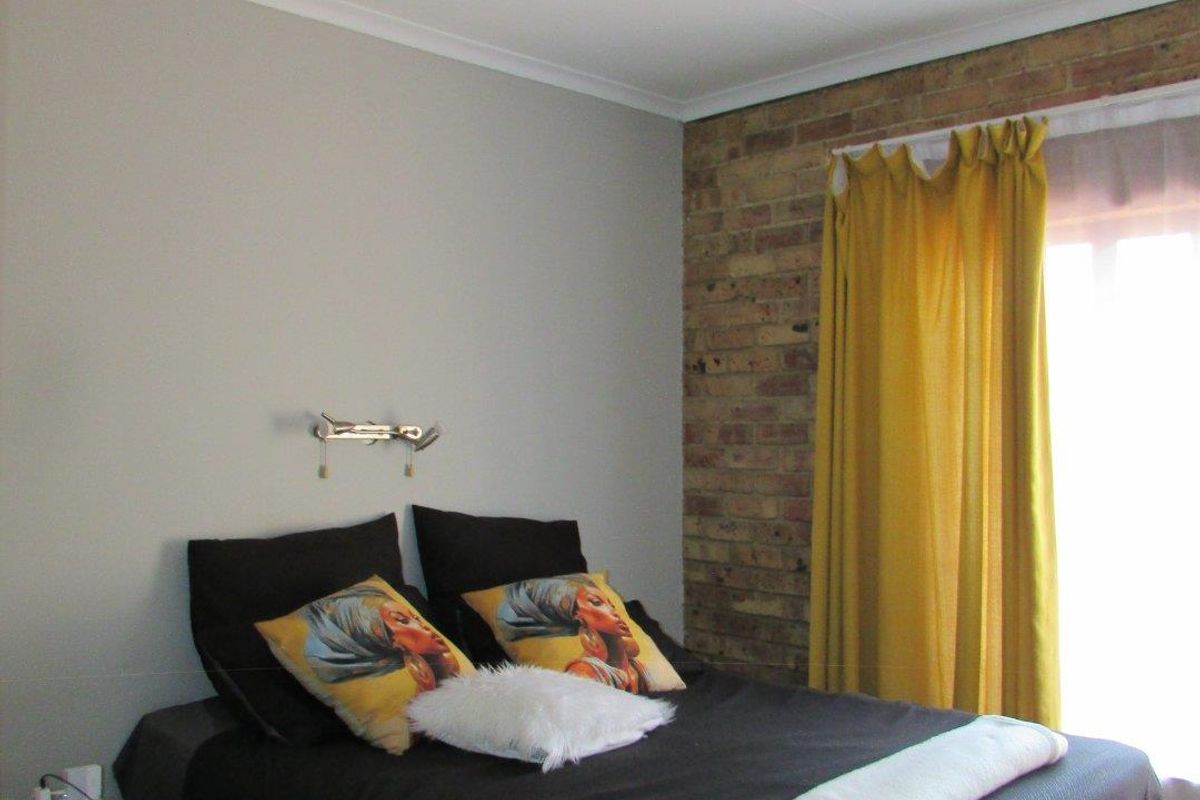 A bedroom featuring a distinctive exposed brick feature wall, tiled flooring, and a window with curtain treatments.