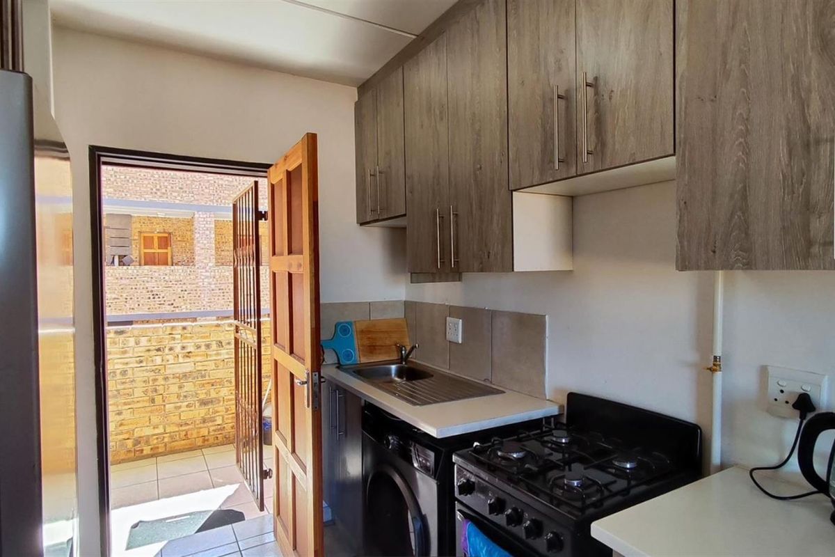 Compact kitchen featuring wood-look cabinetry, a stainless steel sink, and a freestanding gas stove, with direct access to an outdoor area.
