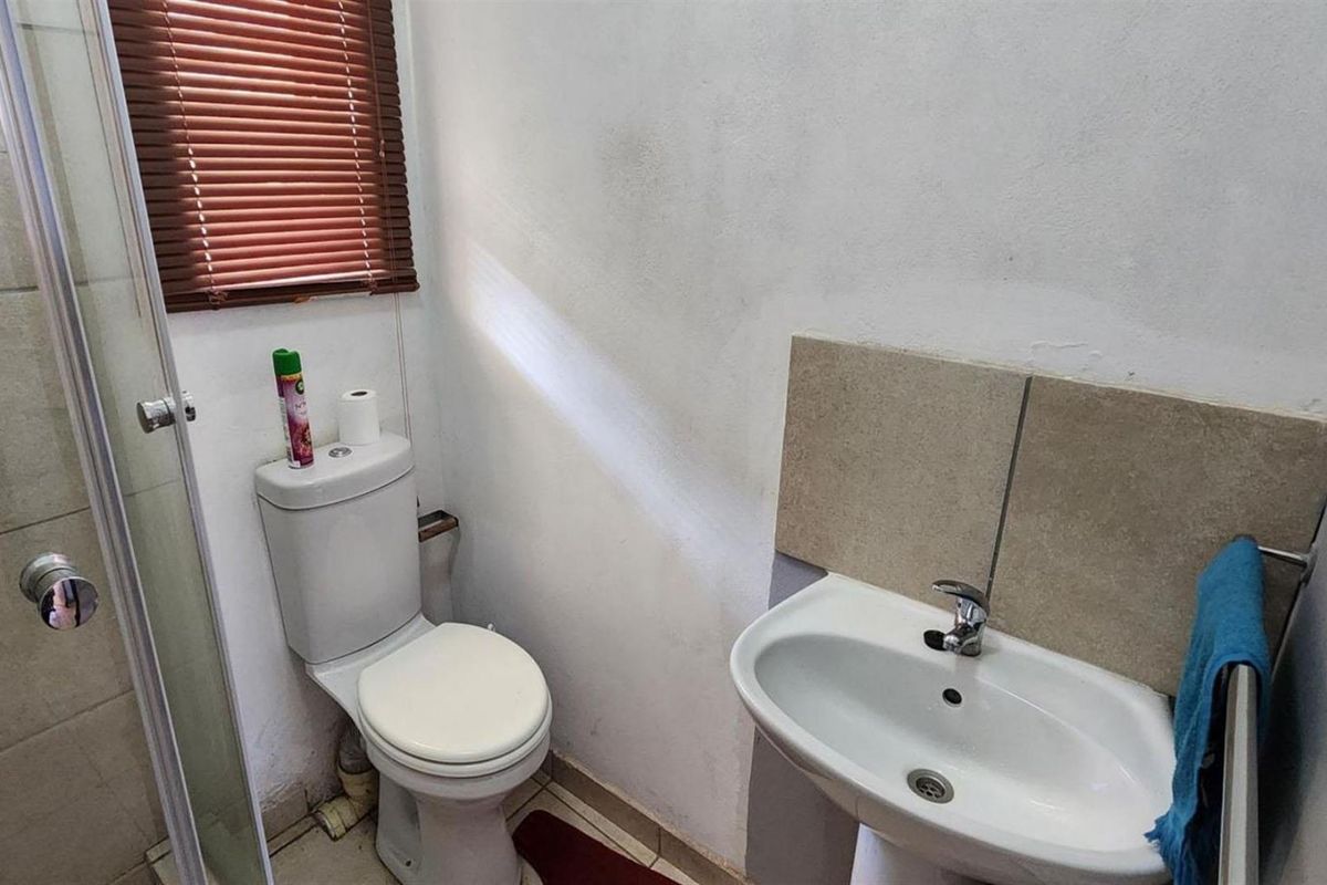 A compact bathroom featuring a pedestal basin, a standard toilet, and a glass-enclosed shower unit with a window blind.
