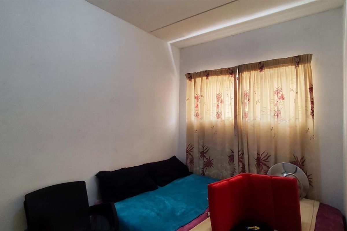 A simple bedroom featuring plain walls and a window with curtains, providing a functional space for rest.