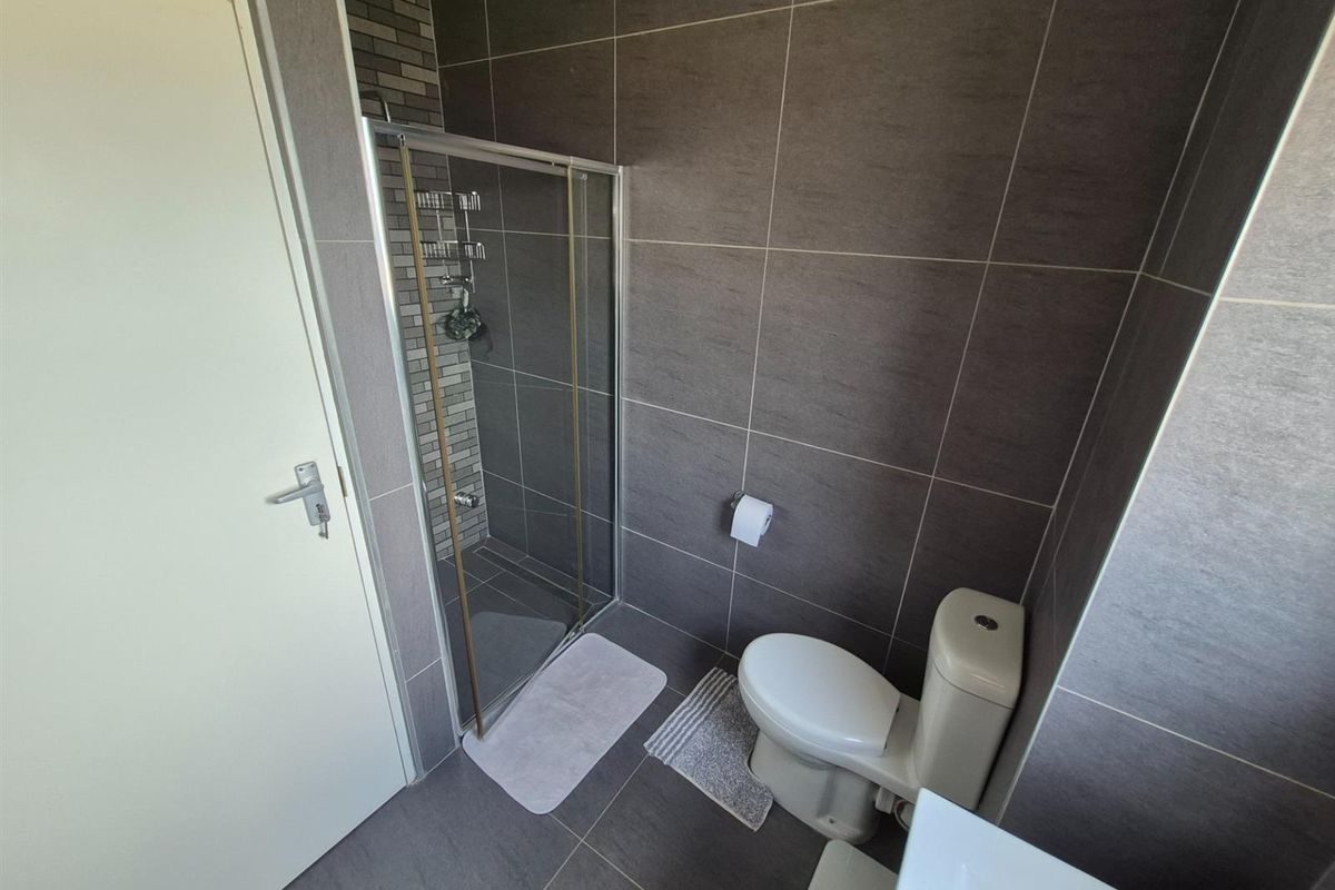 A modern bathroom featuring dark grey wall and floor tiles, a glass-enclosed shower, and a standard toilet.
