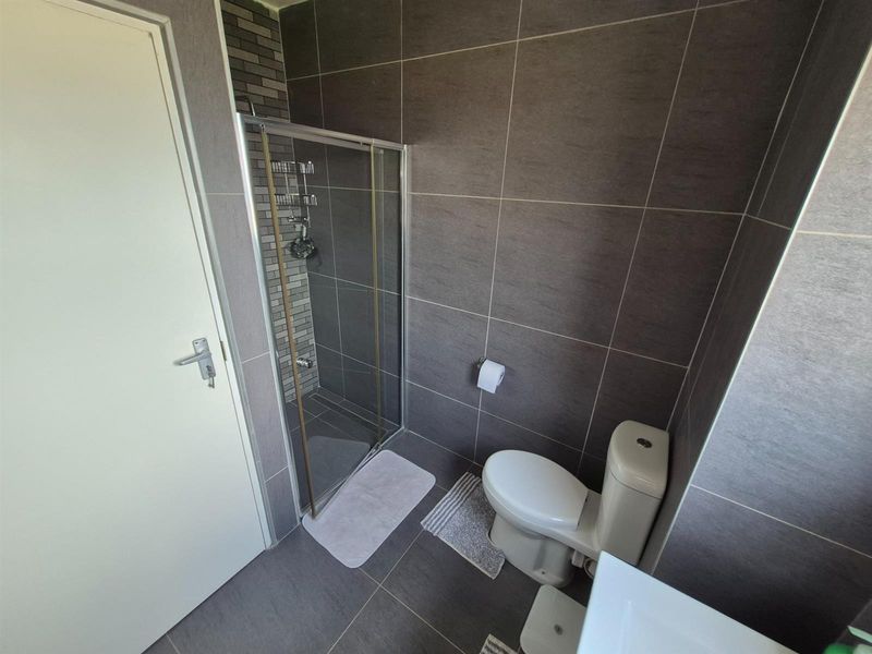 A modern bathroom featuring dark grey wall and floor tiles, a glass-enclosed shower, and a standard toilet.