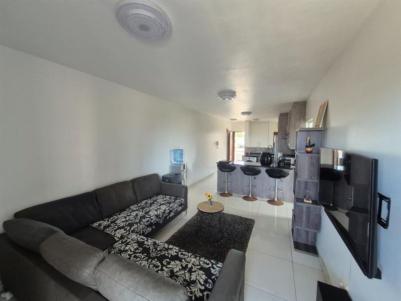 Open-plan living area featuring a modern kitchen with a breakfast bar, sleek cabinetry, and tiled flooring throughout the combined space.
