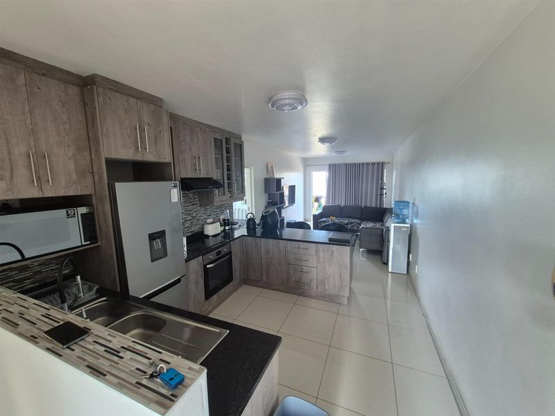 Open-plan kitchen and living area featuring modern wood-grain cabinetry, dark countertops, tiled flooring, and direct access to a balcony.