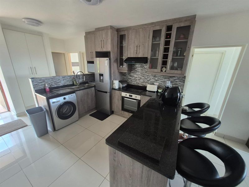 Modern kitchen featuring wood-look cabinetry, granite countertops, a breakfast bar, built-in oven, extractor fan, and integrated laundry plumbing.