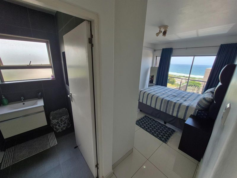 A view from the hallway looking into a modern bathroom with dark tiling and a bedroom featuring large windows with ocean views.