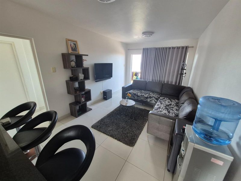 A well-lit open plan living area featuring tiled flooring, neutral walls, and direct access to a balcony through a sliding glass door.