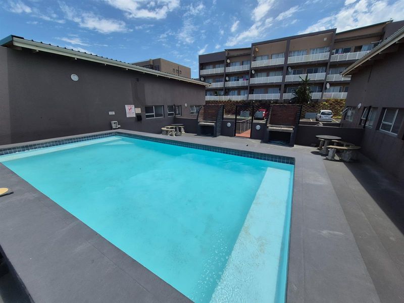 Communal swimming pool area featuring built-in brick braai facilities and paved surround, situated within an apartment complex.