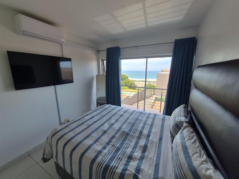 A well-maintained bedroom featuring a wall-mounted air conditioning unit, tiled flooring, and sliding glass doors that open to a balcony with ocean views.