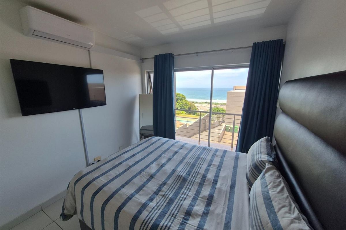 A well-maintained bedroom featuring a wall-mounted air conditioning unit, tiled flooring, and sliding glass doors that open to a balcony with ocean views.