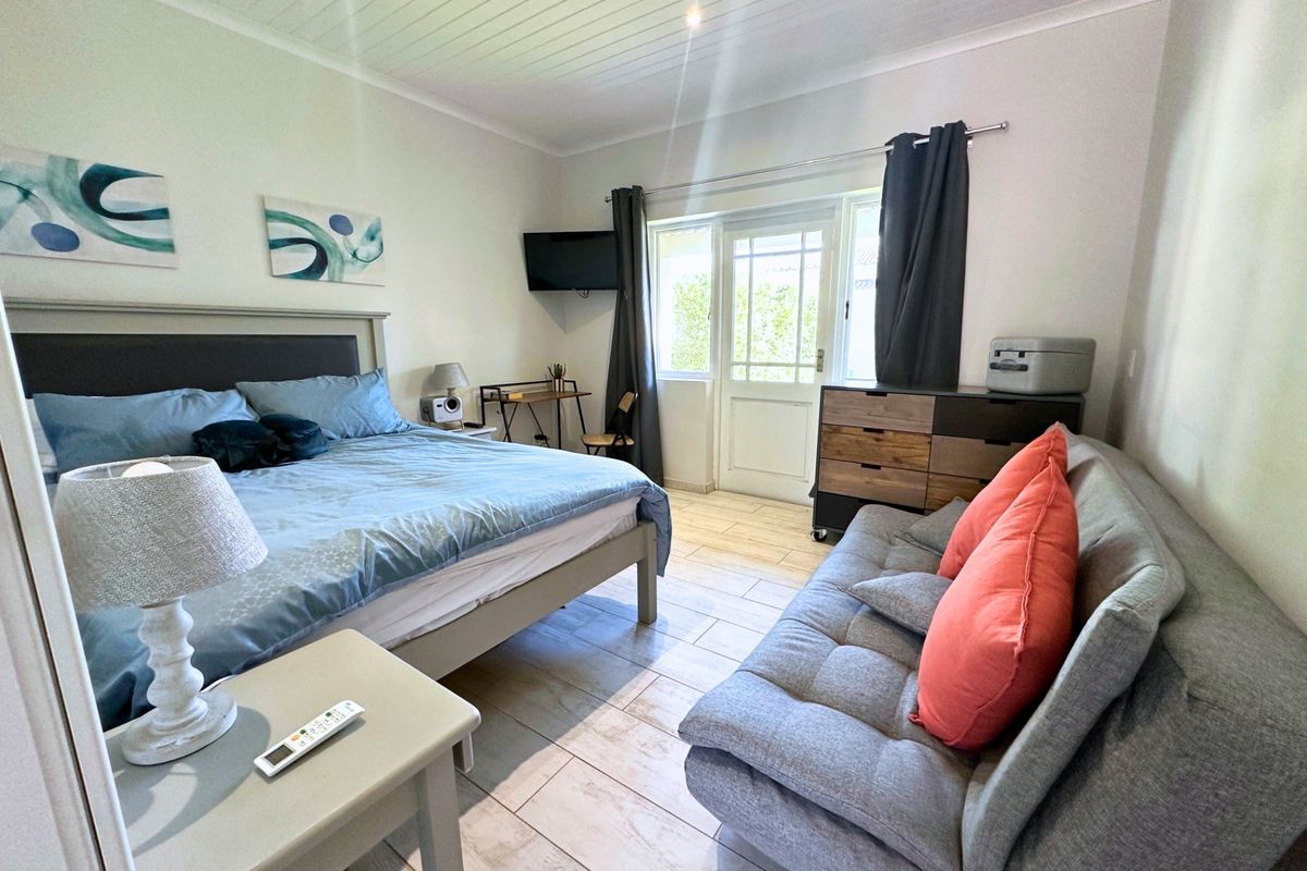 A well-maintained bedroom featuring light-toned tiled flooring, a white tongue and groove ceiling, and direct access to the outdoors via a glass-panelled door.