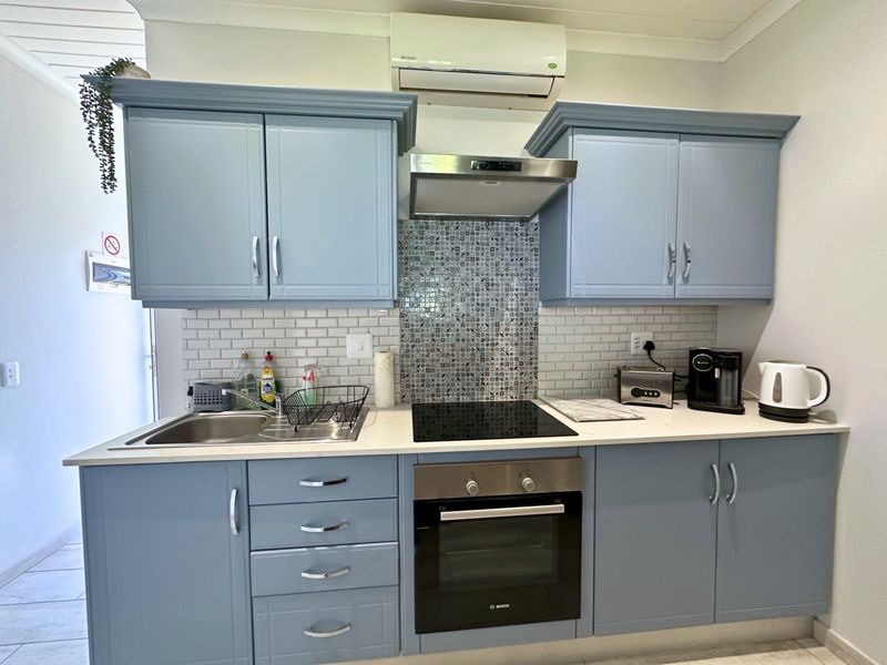 A compact, well-maintained kitchen featuring blue cabinetry, a subway tile backsplash, integrated oven and hob, and a wall-mounted air conditioning unit.
