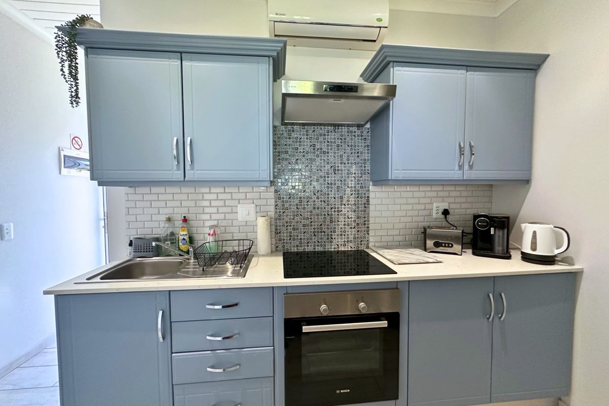 A compact, well-maintained kitchen featuring blue cabinetry, a subway tile backsplash, integrated oven and hob, and a wall-mounted air conditioning unit.