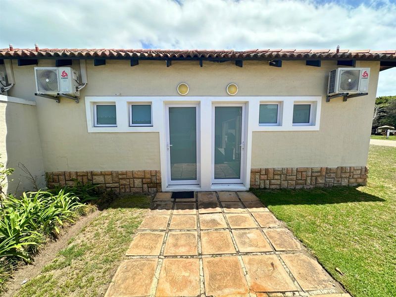 Rear exterior view of the property featuring stone cladding, dual glass entry doors, and mounted air conditioning units with a paved walkway.