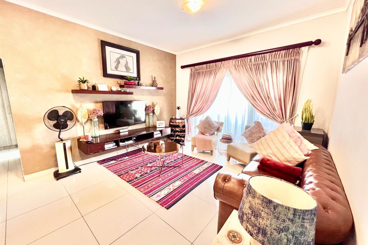 A well-lit living room featuring large format floor tiles, a feature wall with floating shelving, and direct access to a balcony through sliding doors.