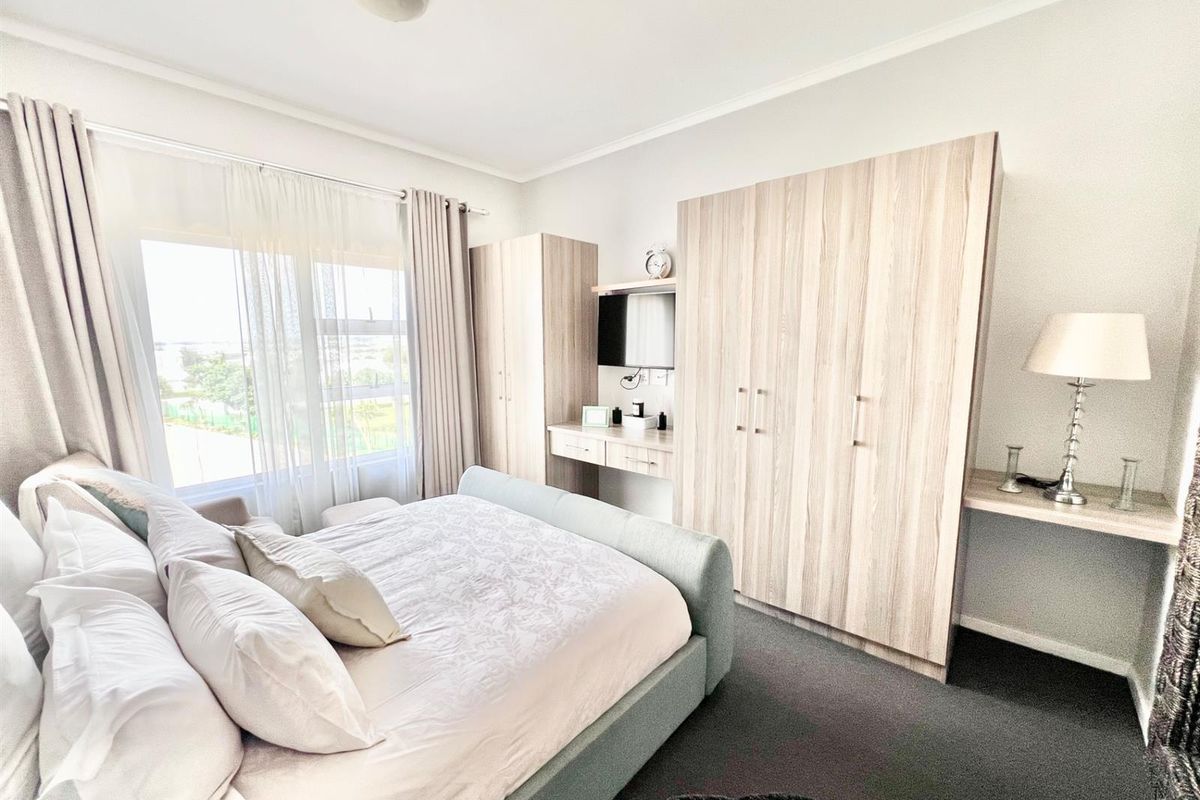 A well-lit bedroom featuring built-in light wood cabinetry, integrated vanity space, and large windows allowing for natural light.