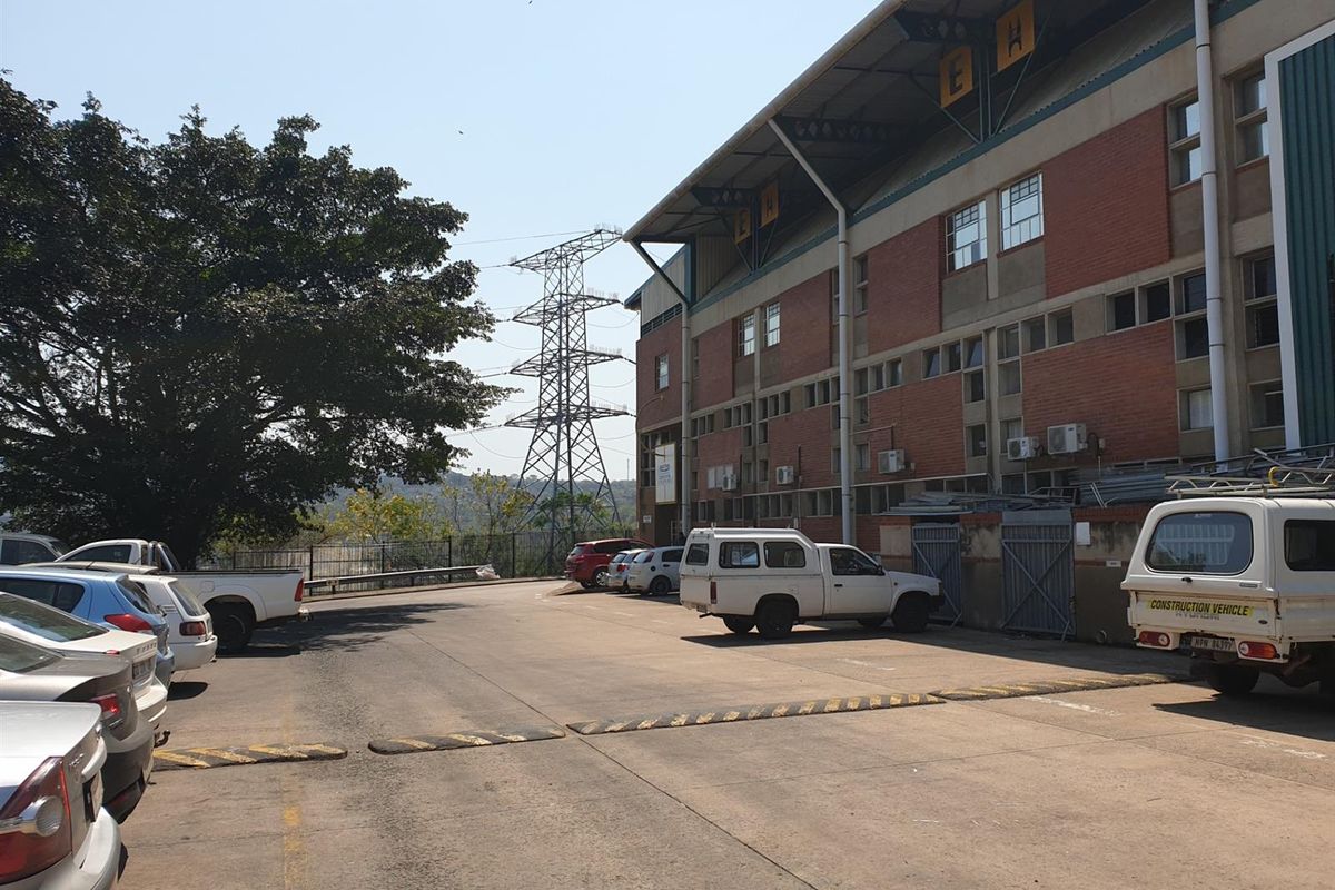 Exterior view of an industrial facility featuring a multi-story brick building, paved parking area, and perimeter fencing.