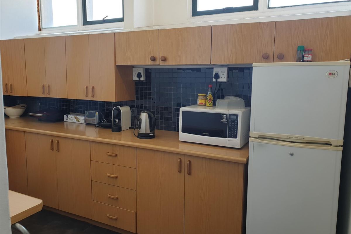 A functional kitchenette featuring wood-look cabinetry, dark tiled backsplash, and ample counter space, suitable for an industrial office or utility area.