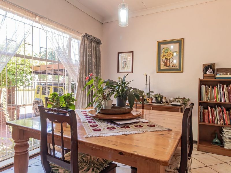 A dining room featuring tiled flooring, a large window with a security gate, and a central pendant light fixture.