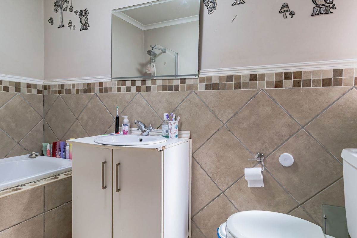 A functional bathroom featuring a built-in vanity, tiled splashback, bathtub, and toilet, with some visible wear on the vanity cabinet.