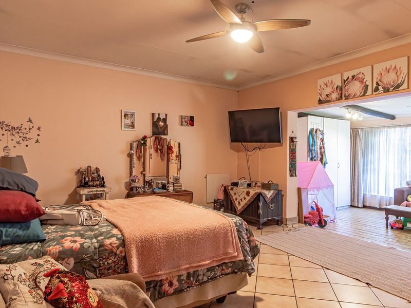 Spacious bedroom featuring tiled flooring, a ceiling fan, and an adjoining sunroom or seating area with large windows.