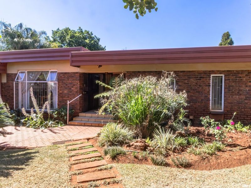 Front elevation of a single-story brick house featuring a paved entrance path, established garden beds, and secure window fixtures.