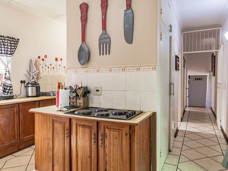 A functional kitchen featuring wooden cabinetry, a built-in electric hob, tiled backsplash, and tiled flooring, leading into a hallway.