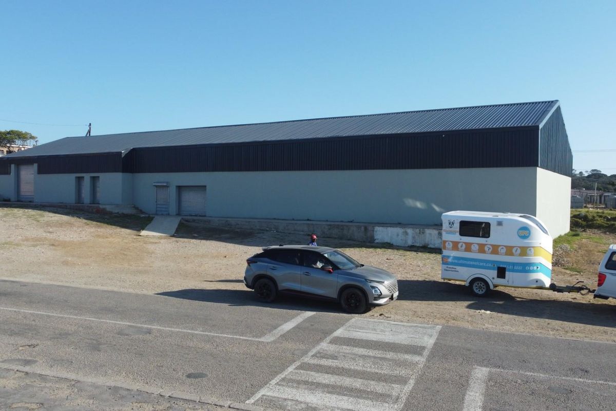 Aerial view of a large industrial retail warehouse building featuring a metal roof and roller shutter doors, situated on a gravel lot.