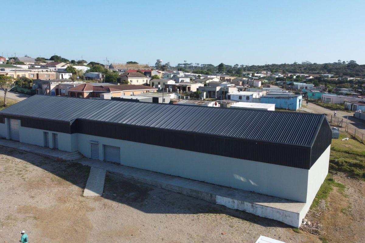 Aerial view of a large rectangular retail warehouse building featuring a modern metal roof and light-colored exterior walls situated in a residential area.