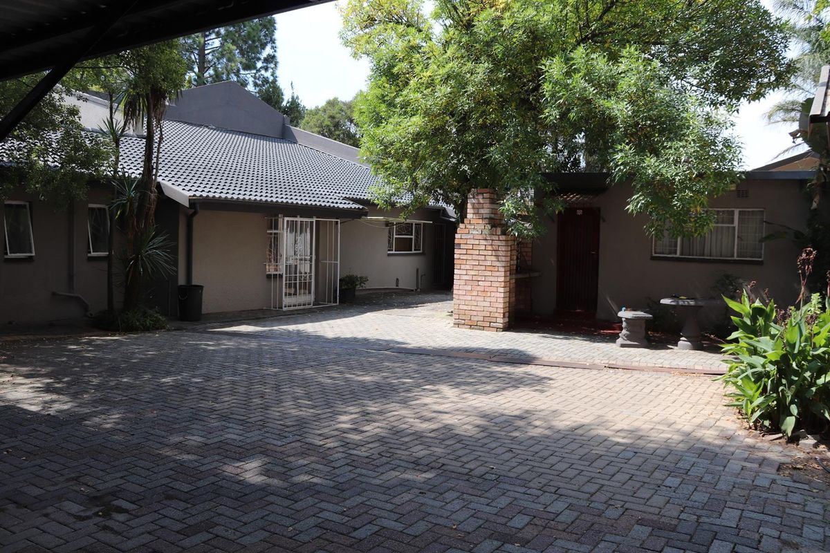 A paved courtyard area featuring a built-in brick braai, mature trees, and access to the main house structure.