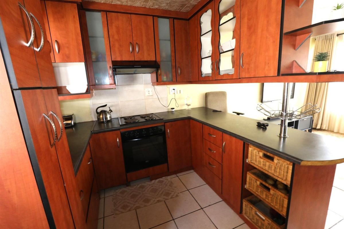 Compact kitchen featuring cherry-wood cabinetry, dark laminate countertops, built-in oven, electric hob, and an integrated extractor fan.